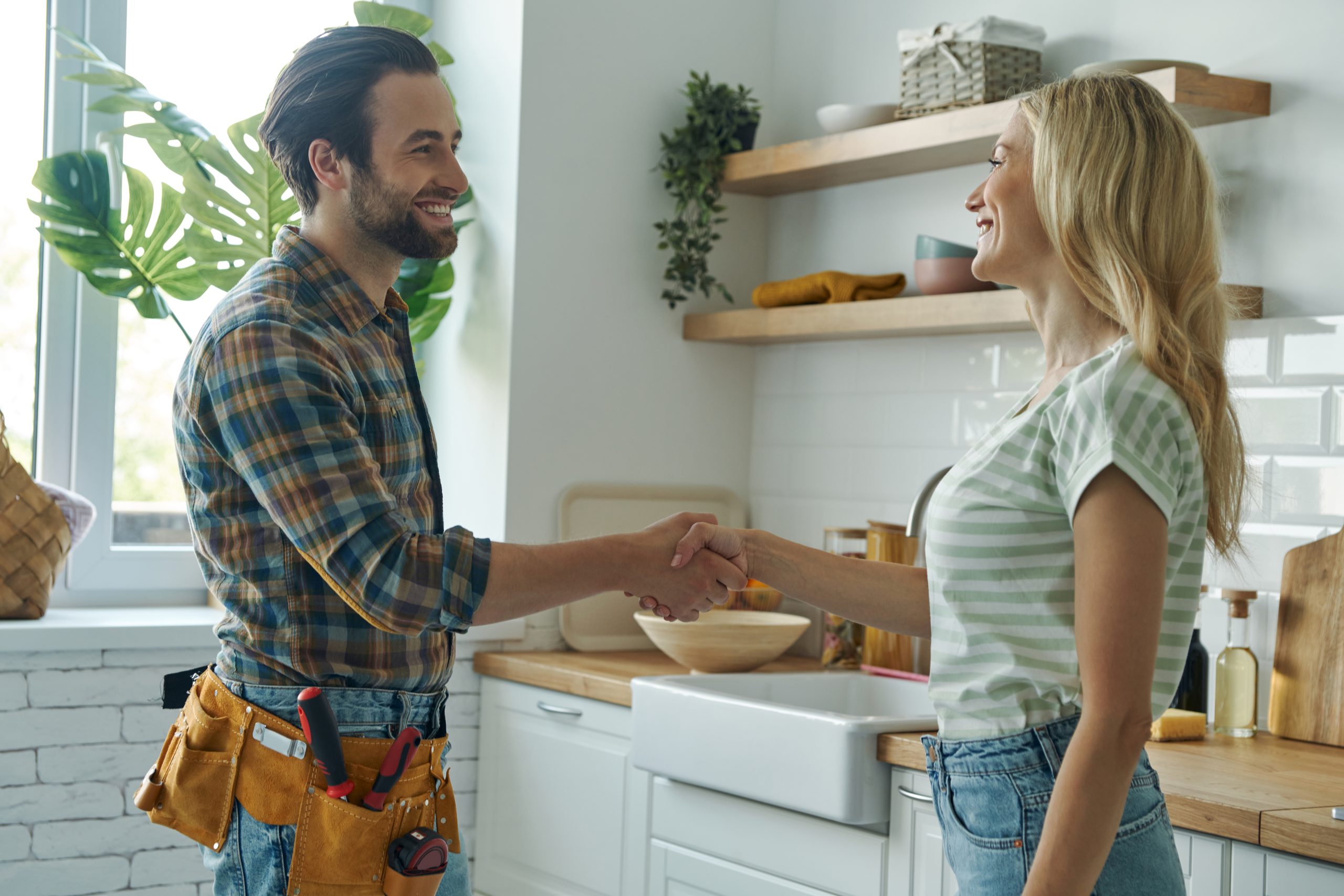 beautiful young woman shaking hand to male plumber while standin