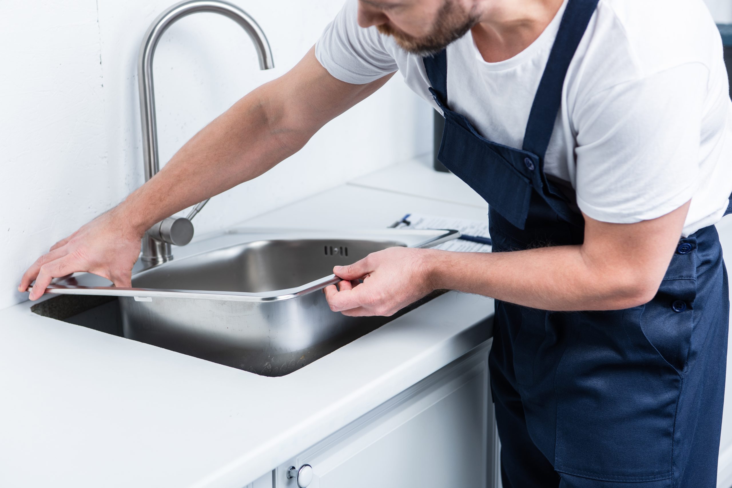 partial view of bearded repairman in working overall fixing sink in kitchen