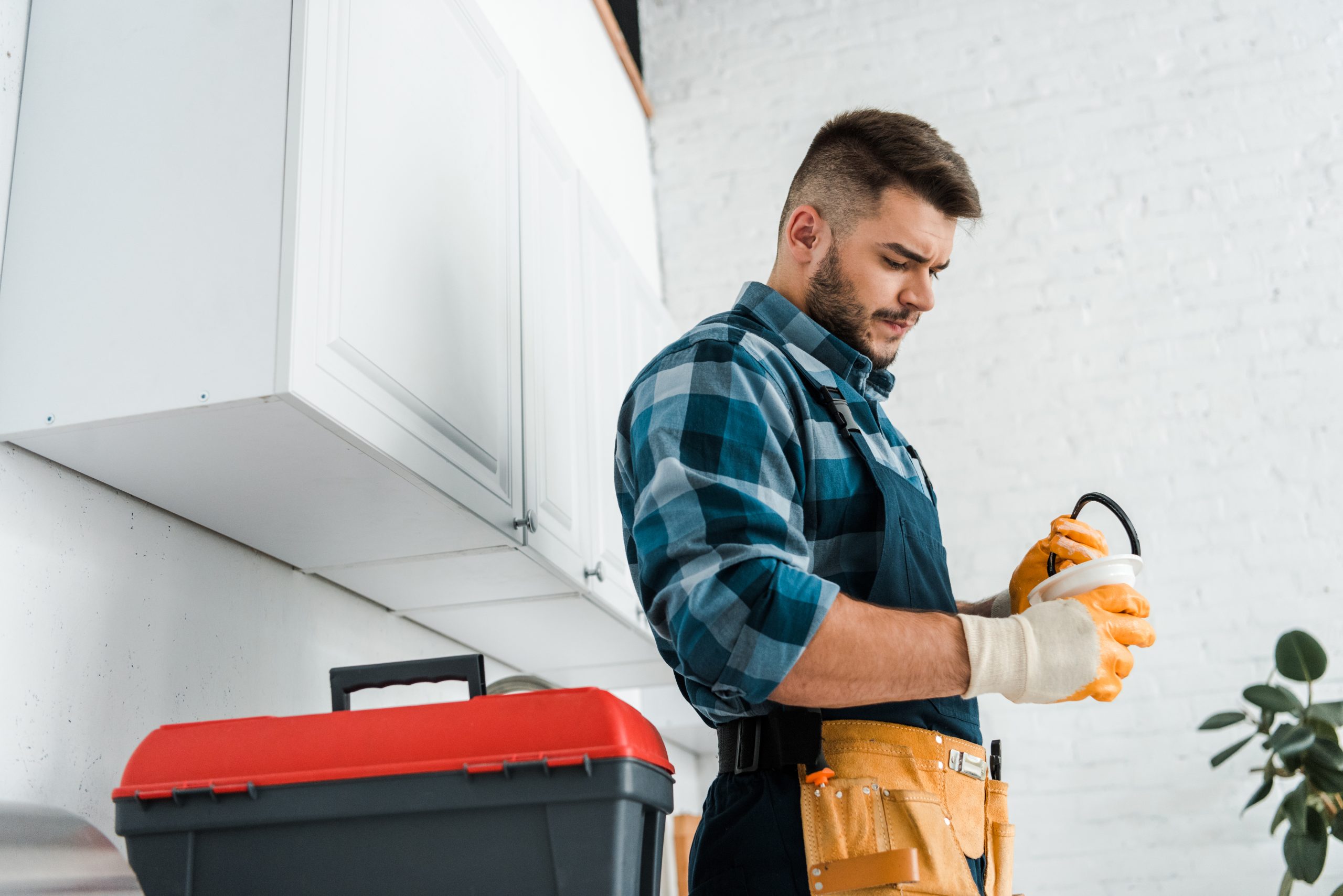 handsome bearded man holding funnel near toolbox in kitchen